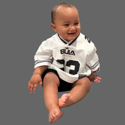 Child wearing a sports jersey sitting on a couch in a living room.