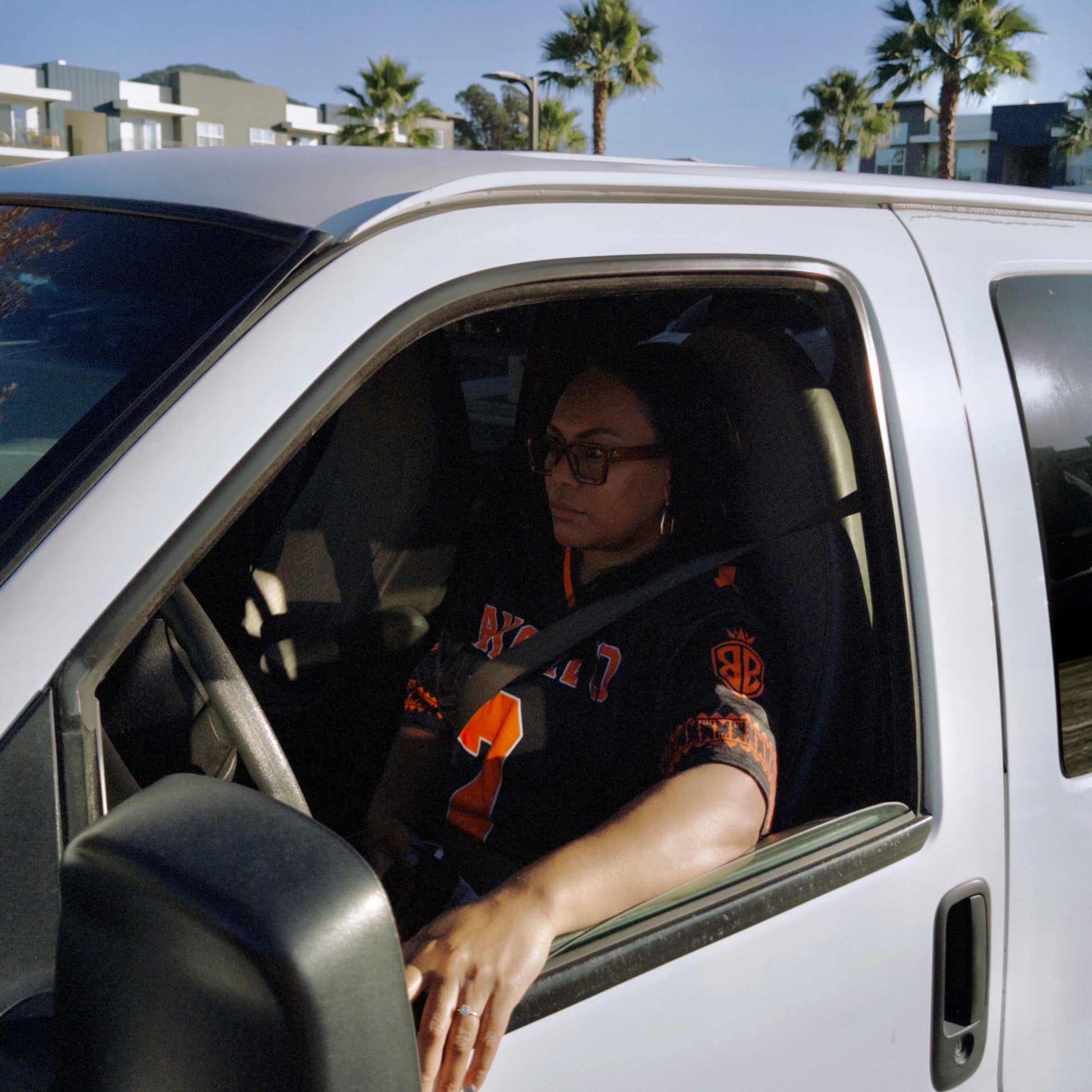 Person sitting inside a white truck with palm trees and buildings in the background